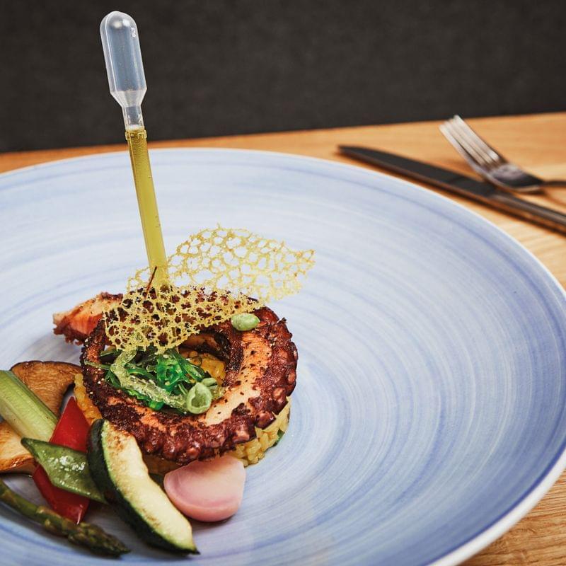 Gourmet octopus dish with vegetables and decorative garnish on blue plate